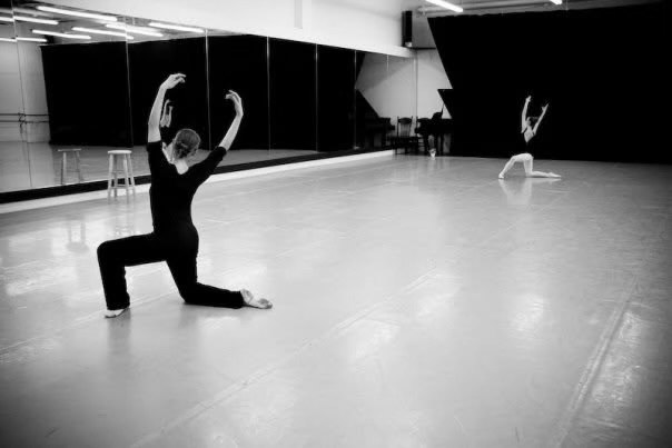 A dancer kneeling with arms raised in a spacious studio